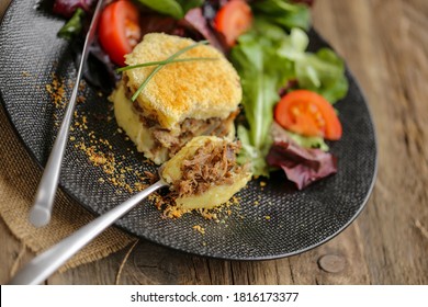 duck shepherd's pie  with mesclun salad on a modern black plate on wooden table 