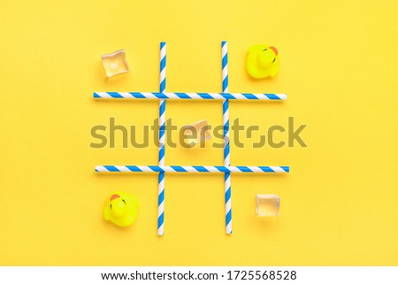duck toy, ice cubes, paper tubes with blue stripes for drinks on a yellow background. Sea battle, tic tac toe game concept Creative composition Flat lay Top view