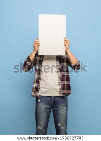 Dude with sign. Young Caucasian man in casual clothes with white blank sheet of paper for copyspace for text or ad isolated on blue background. Concept of human emotions, fun, sales, daily life.
