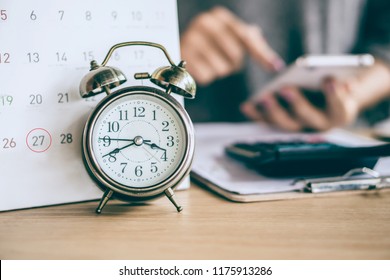 due date calendar and alarm clock with blur business woman hand calculating  monthly expenses during tax season.