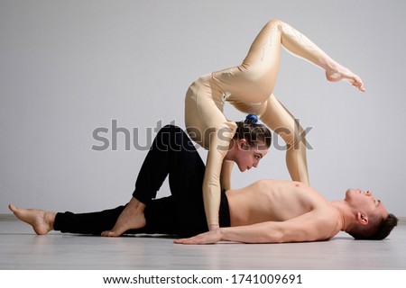 A duet of acrobats showing a pair trick. A woman in gymnastics overalls in a handstand over a shirtless man lies on his back. Very flexible circus performers.