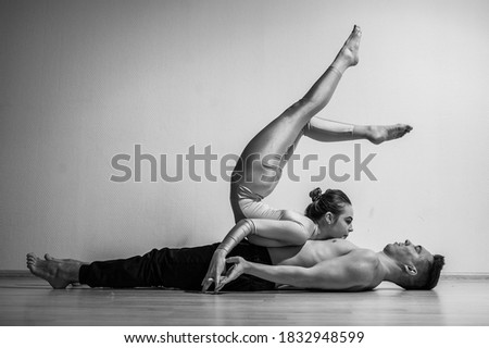 A duet of acrobats showing a pair trick. A woman in gymnastics overalls in a handstand over a shirtless man lies on his back. Very flexible circus performers.