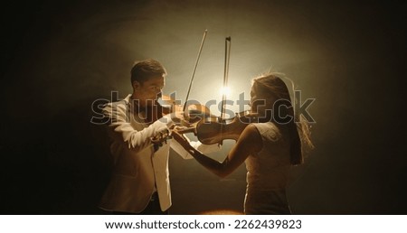 Duet of two professional violin players having a solo together, performing on stage during concert, spotted by light on black background 