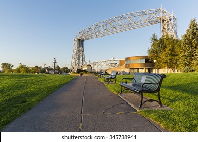 Duluth Canal Park - A sidewalk with park benches leading toward a lift bridge.