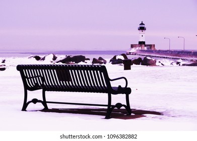 Duluth Minnesota Lighthouse Canal Park Harbor Near Bridge Wintertime Photo With Snow And Ice With Park Bench In Foreground And Dark Shadow Purple Tone