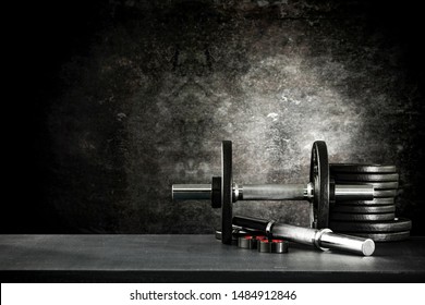 Dumbbell, Barbell And Workout In The Gym. Copy Space On Black Grunge Wall And Board Background.