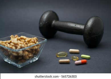 Dumbbell, Walnuts And Dietary Supplements On Dark Background: Fitness And Muscle Building Concept.