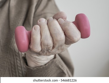 Dumbbells, Closeup Wrinkled Hand Of Old Senior Man Or Woman Or Person Holding Pink Small Dumbbell To Sport Exercise Or Be Fit. Geriatric Old People Health Concept Photo. Senior People Body Part, Hand