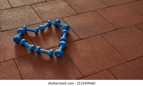 Dumbbells In Form Of Heart On Floor In Sunny Gym. Sports Items For Bodybuilding, Fitness And Exercising. Equipment For Pumping Body And Healthy Lifestyle. Sports Center. Background For Copy Space