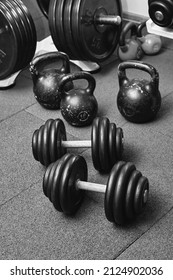 Dumbbells And Kettlebells On A Floor. Bodybuilding Equipment. Fitness Or Bodybuilding Concept Background. Black And White Photography