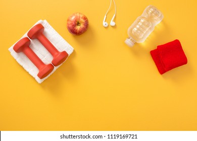 Dumbbells, Towel, Headphones, Apple, Water Bottle And Wrist Bands. Fitness Flatlay, On Yellow Background With Copy Space.