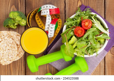 Dumbells, Tape Measure And Healthy Food Over Wooden Table. Fitness And Health