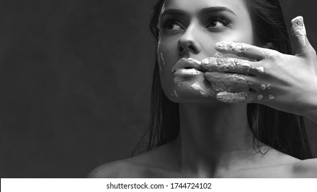 Dumbness and inability to speak about problems and thoughts, concept. Portrait of a young sensual woman with paint or clay on her face, shut up and close her mouth. Sad black and white portrait