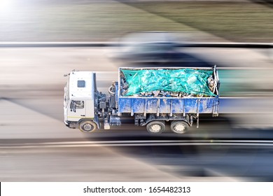 dump truck for building waste disposal transportation in motion against blurred road background. Aerial top down view of moving vehicle with industrial waste container bin. Trash car from above