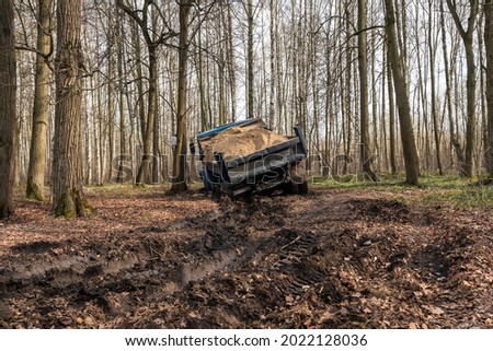 Dump truck car stuck in mud on the road among trees. Blurry mud bad road in the park. Тruck dump car with sand stopped due to wet dirty on its way to park.