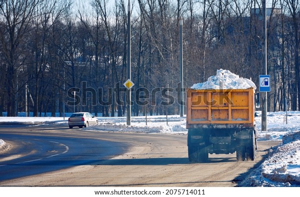 Dump truck full of\
snow driving through city street, snow hauling. Dump truck\
transports snow to dump site.\
