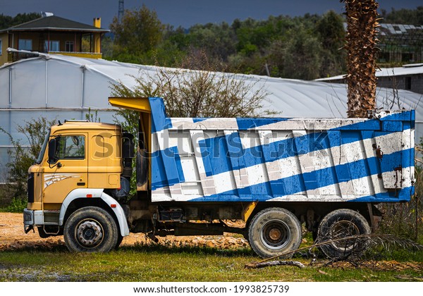 Dump truck with the image of the national flag of\
Greece is parked against the background of the countryside. The\
concept of export-import, transportation, national delivery of\
goods