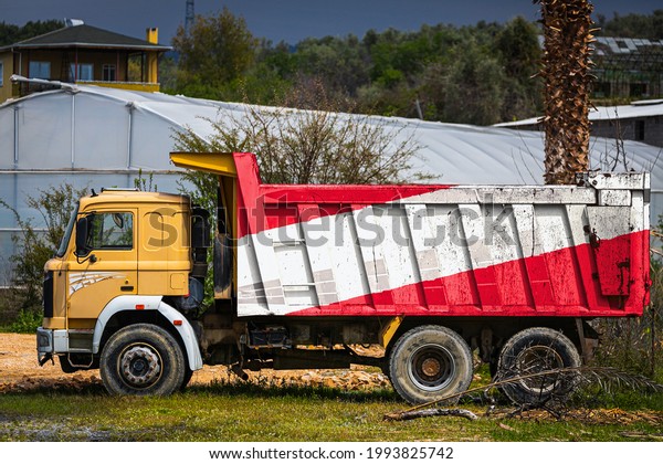 Dump truck with the image of the national flag of\
Austria is parked against the background of the countryside. The\
concept of export-import, transportation, national delivery of\
goods
