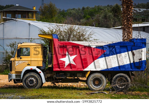 Dump truck\
with the image of the national flag of Cuba is parked against the\
background of the countryside. The concept of export-import,\
transportation, national delivery of\
goods