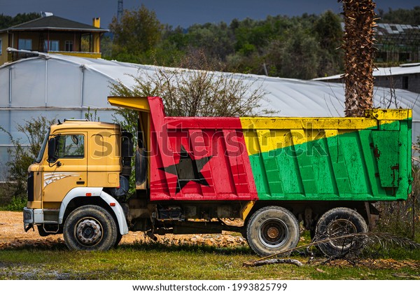 Dump truck with the image of the national flag of\
Guinea Bissau is parked against the background of the countryside.\
The concept of export-import, transportation, national delivery of\
goods