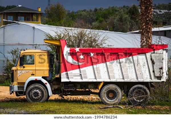 Dump truck with the image of the national flag of\
Singapore is parked against the background of the countryside. The\
concept of export-import, transportation, national delivery of\
goods
