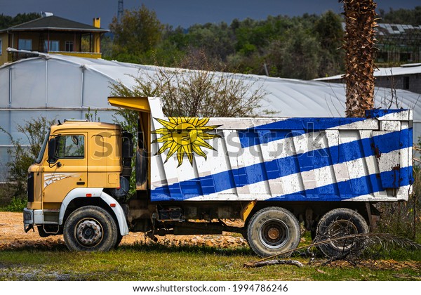 Dump truck with the image of the national flag of\
Uruguay is parked against the background of the countryside. The\
concept of export-import, transportation, national delivery of\
goods