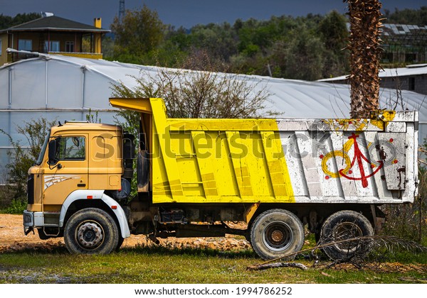 Dump truck with the image of the national flag of\
Vatican is parked against the background of the countryside. The\
concept of export-import, transportation, national delivery of\
goods