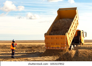Dump truck is moving down sand on construction site. Leveling the ground. Signalman on construction site to assist dump truck driver to move down sand. 