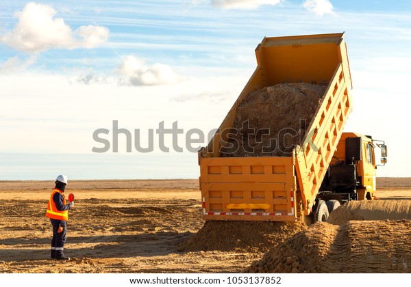 Dump truck is moving down sand on\
construction site. Leveling the ground. Signalman on construction\
site to assist dump truck driver to move down sand.\

