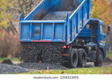 Dump truck, tractor and bulldozer unloading gravel, road metal, rubble and crushed stone cement material during landscaping improvement and new pedestrian walk path road construction site