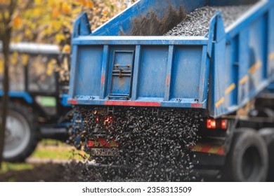 Dump truck, tractor and bulldozer unloading gravel, road metal, rubble and crushed stone cement material during landscaping improvement and new pedestrian walk path road construction site