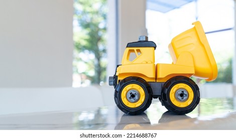 Dump Truck, Yellow Construction Toy Vehicle With Articulated Parts Built With Sturdy Plastic Is Placed On A Table.