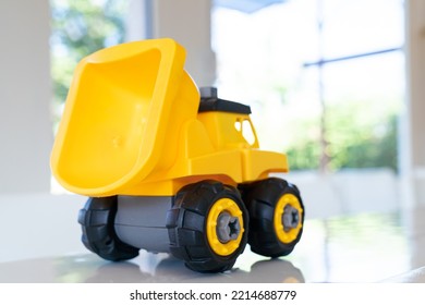 Dump Truck, Yellow Construction Toy Vehicle With Articulated Parts Built With Sturdy Plastic Is Placed On A Table.