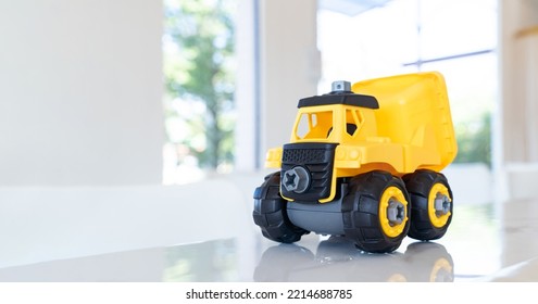 Dump Truck, Yellow Construction Toy Vehicle With Articulated Parts Built With Sturdy Plastic Is Placed On A Table.