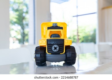 Dump Truck, Yellow Construction Toy Vehicle With Articulated Parts Built With Sturdy Plastic Is Placed On A Table.