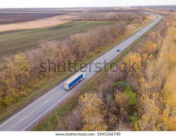 Dump trucks carrying goods on the highway.\
Greeen trucks driving on asphalt road along the forest seen from\
the air. Aerial view\
landscape.