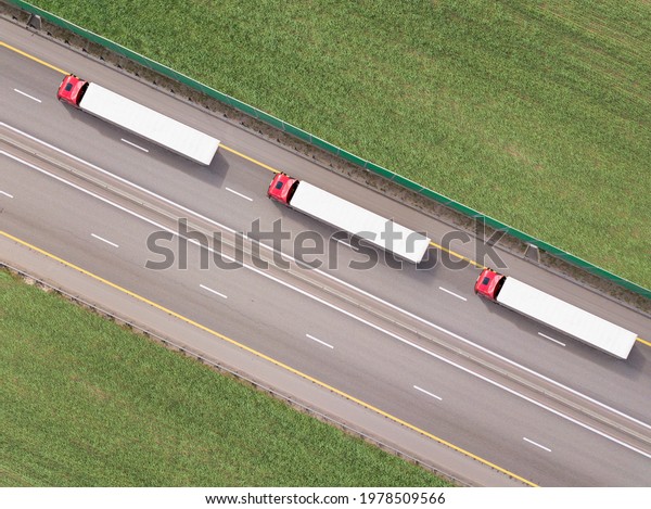 Dump trucks\
carrying goods on the highway. Red truck driving on asphalt road\
along the green fields. seen from the air. Aerial view landscape.\
drone photography. cargo\
delivery