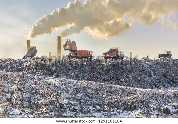 Dump trucks\
unloading garbage over vast landfill. Smoking industrial stacks on\
background. Environmental pollution. Outdated method of waste\
disposal. Survival of times\
past