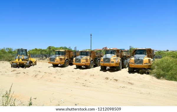 Dump trucks and yellow\
bulldozer parked in the sand ready for maintenance work on the\
beach.