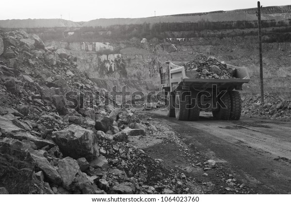 Dump-body truck loaded with ore moves along\
the road in a quarry, back view, black and white. Mining industry.\
Mine and quarry\
equipment.
