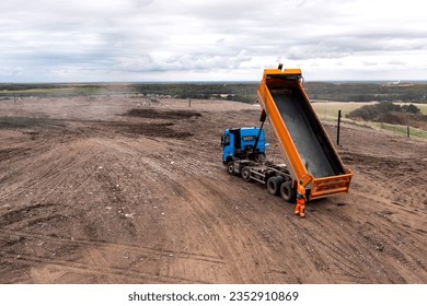 A dumper truck driver lowering the trailer of a timmper truck after unloading waste at a large landfill waste dump with copy space - Powered by Shutterstock