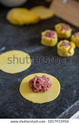 Dumpling making, shumai asian dumpling in progress, dumpling wrapper with pork and shrimp filling ready to fold on a dark kitchen counter with ready dumplings in the background