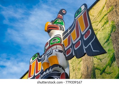 DUNCAN, BC, CANADA - DEC 8, 2017: View of ancient colorful Totem Pole with blue sky and painted mural behind it, taken in Duncan, British Columbia, Canada.