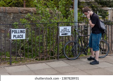 Dundee, Scotland/United Kingdom - May 3 2019: Man With Bicycle Speaking On A Phone Outside A Polling Station During An Election In The United Kingdom