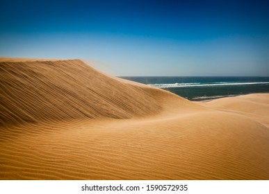 Dune meets Sea. Large sand dune being blown by the wind toward the ocean.
