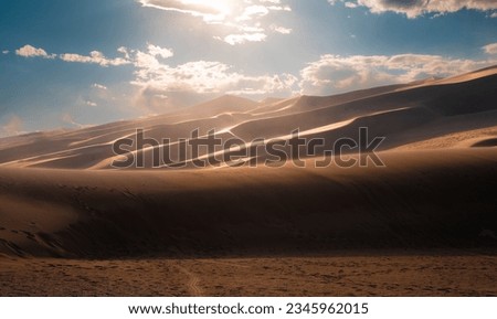 dunes in the desert with a cloudy day, blue sky and foot prints.