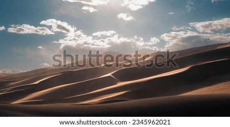 dunes in the desert with a cloudy day, blue sky and foot prints.