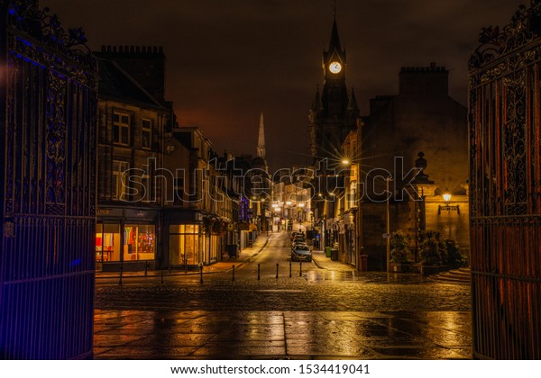 Dunfermline town centre, fife, scotland\
at night with low ambient light. cars parked up with shops and pubs\
in view, clock tower and night sky. Taken\
09/16/2019