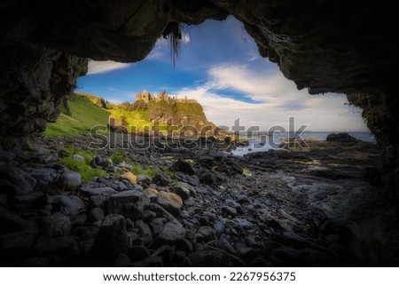 Dunluce Castle seen from a small cave on a shoreline, nested on the edge of cliff, part of Wild Atlantic Way, Bushmills, Northern Ireland. Film location of poular TV show Game of Thrones