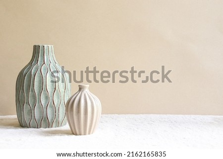 Duo of vases on a beige background. A medium sized sky blue vase with brown grooves and a small beige vase. 